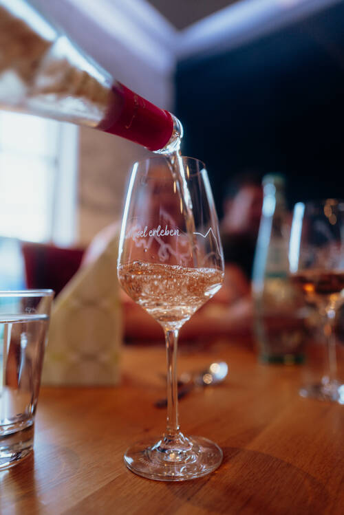 Roséwein wird aus einer Flasche in ein Weinglas auf einem gedeckten Tisch eingeschenkt.