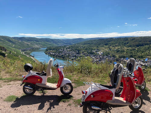 Drei rote Motorroller, die in den Weinbergen abgestellt wurden. Im Hintergrund sieht man die Moselschleife bei Wehlen und den strahlend blauen Himmel.