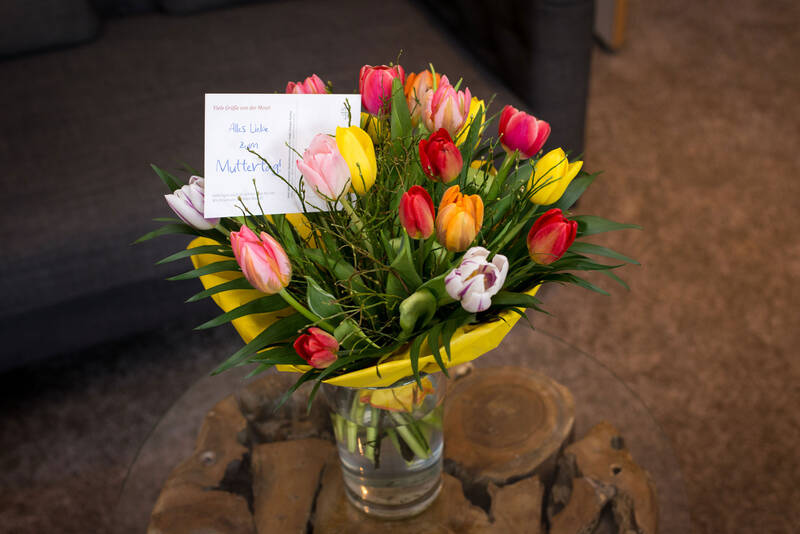 Ein bunter Tulpenstrauß steht auf einem Beistelltisch neben einer Couch in der Suite des Hotels Deutschherrenhof. Eine Postkarte mit der Aufschrift „Herzlich Willkommen“ steckt im Strauß.