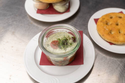 Ein Glas gefüllt mit Aufstrich steht auf einem Teller, daneben liegt ein Teller mit einem Rosmarin-Focaccia.