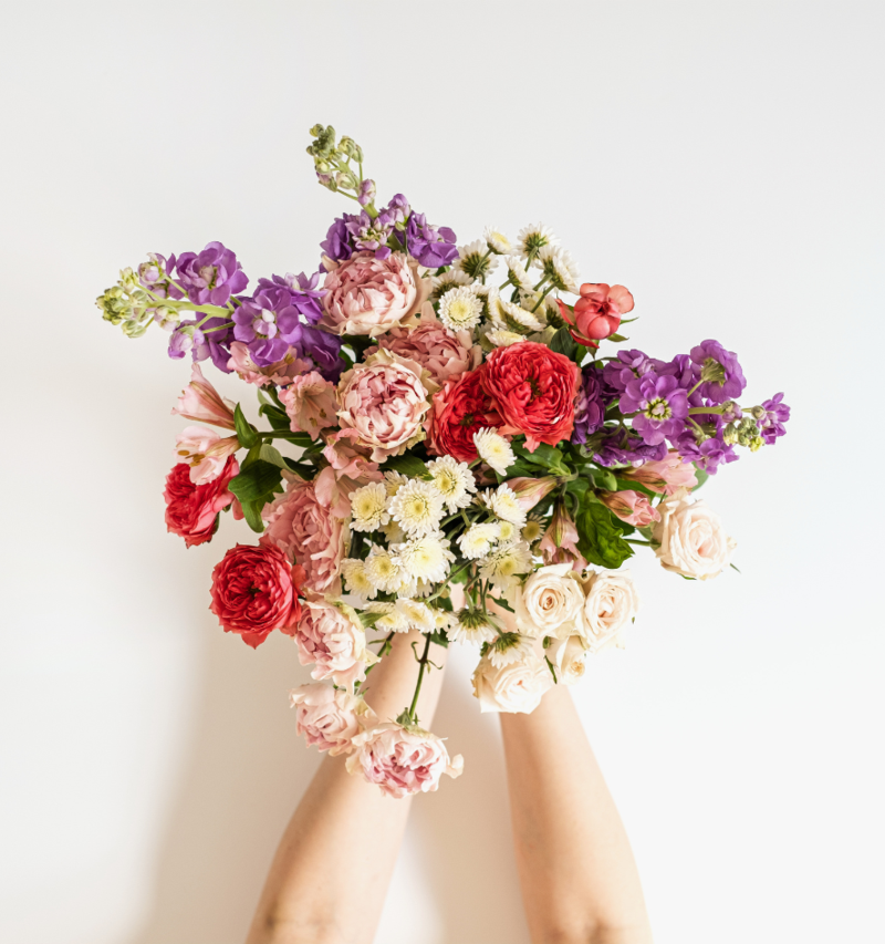 Ein bunter Blumenstrauß wird von zwei Händen ins Bild gestreckt.