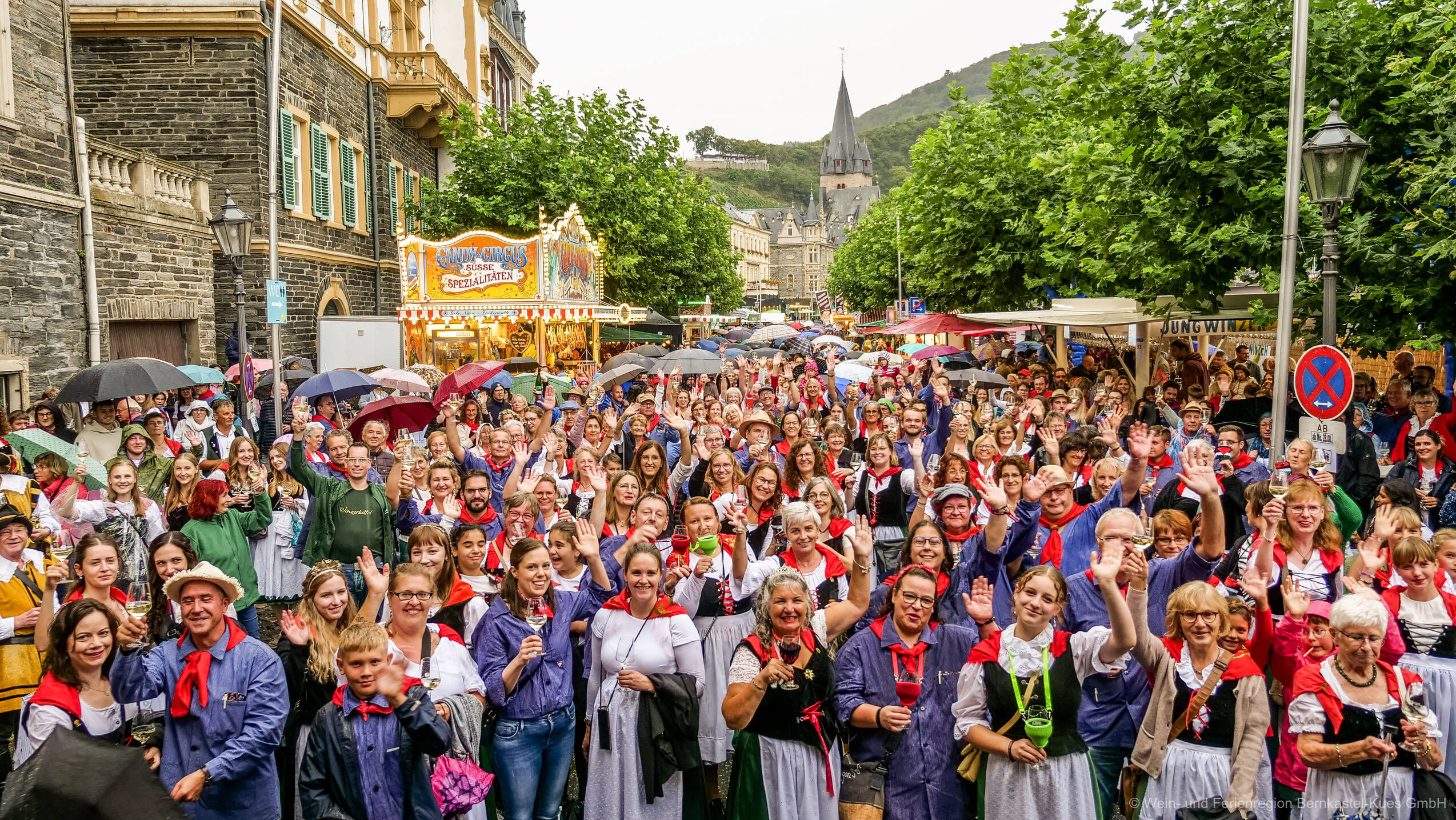 Hunderte Weinfestbesucher in Moseltracht, mit Winzerkitteln und Moselblümchen, versammeln sich auf der Weinstraße vor der Bühne.