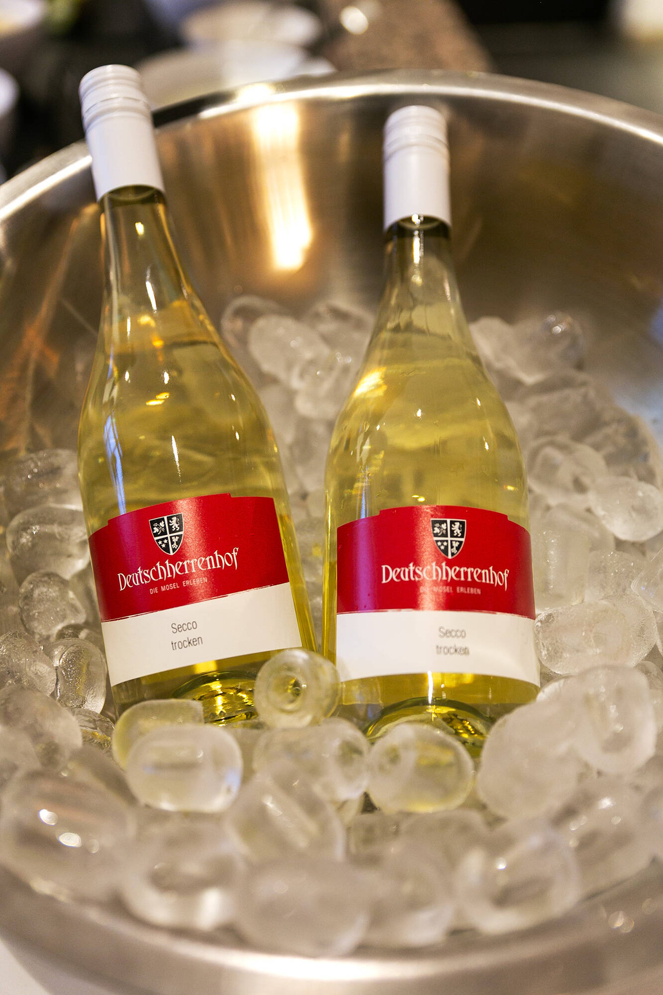In einem großen Sektkühler, gefüllt mit Eiswürfeln, liegen zwei Flaschen Secco, jeweils mit einem Etikett des Deutschherrenhofs.