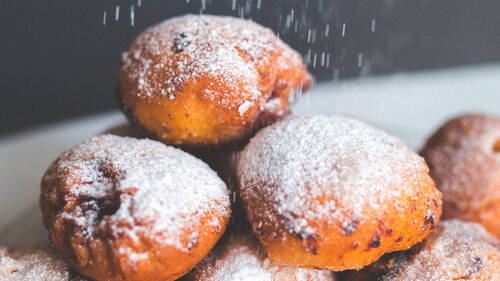 Drei Mäuschen, ein traditionelles Karnevalsgebäck ähnlich wie Quarkbällchen, sind aufeinander gestapelt. Von oben rieselt Puderzucker auf das Gebäck.