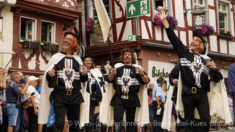 Eine Gruppe der Rachtiger Deutschherren geht in ihren Kostümen über den Marktplatz und grüßt die Menschen freundlich und strahlend.