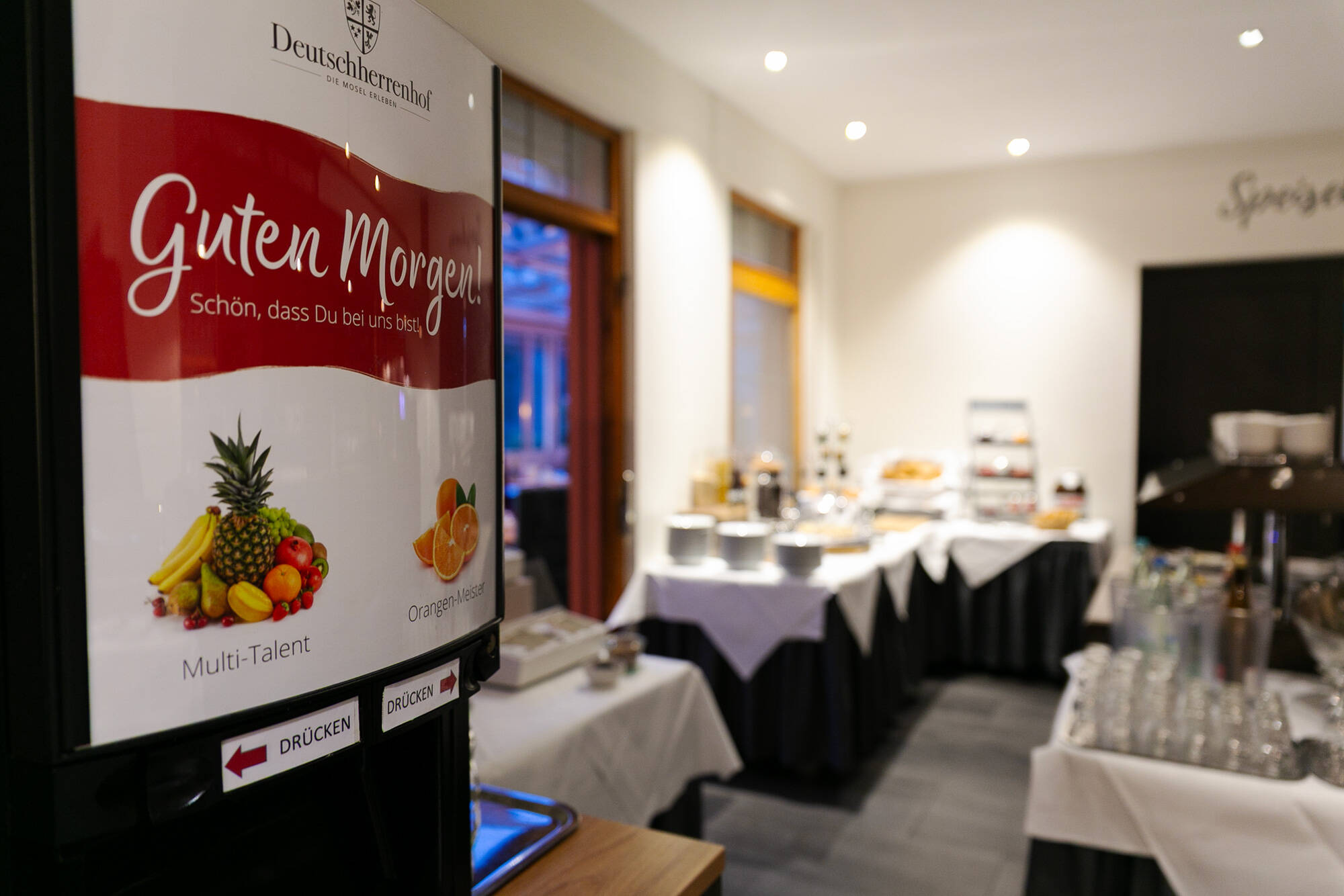 Blick auf das Frühstücksbuffet: Im Vordergrund steht ein Getränkeautomat, auf dem groß "Guten Morgen, schön, dass du da bist" zu lesen ist.