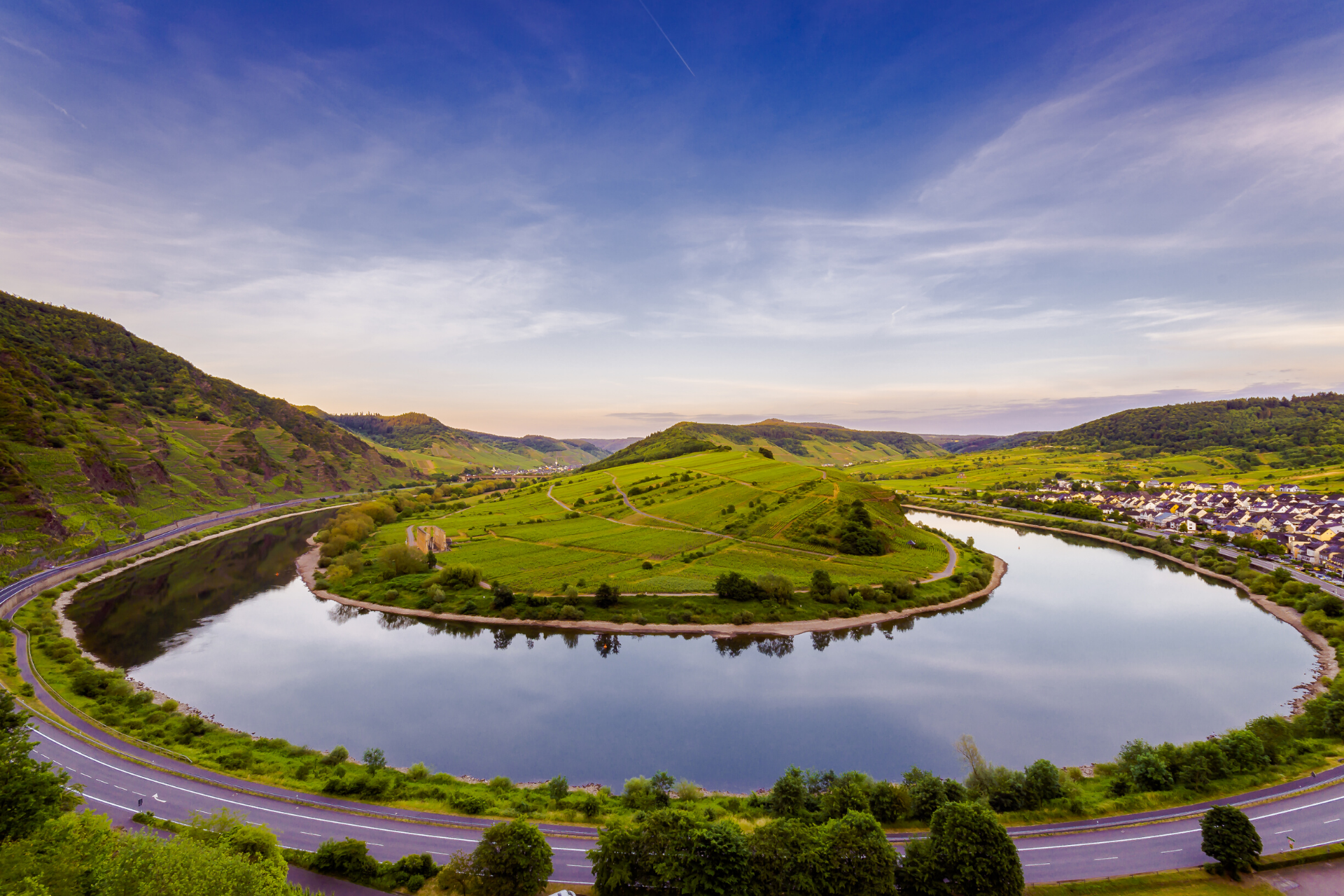 Blick auf die Moselschleife bei Bremm. Das Wasser ist spiegelglatt und reflektiert den strahlend blauen Himmel. Am rechten Bildrand liegt der Weinort Bremm.