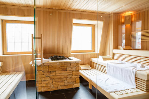 Blick in die Sauna des Deutschherrenhofs. Auf den drei Holzstufen liegen große weiße Handtücher. Durch die Glaswand und Fenster wird die Sauna von natürlichem Licht erleuchtet.