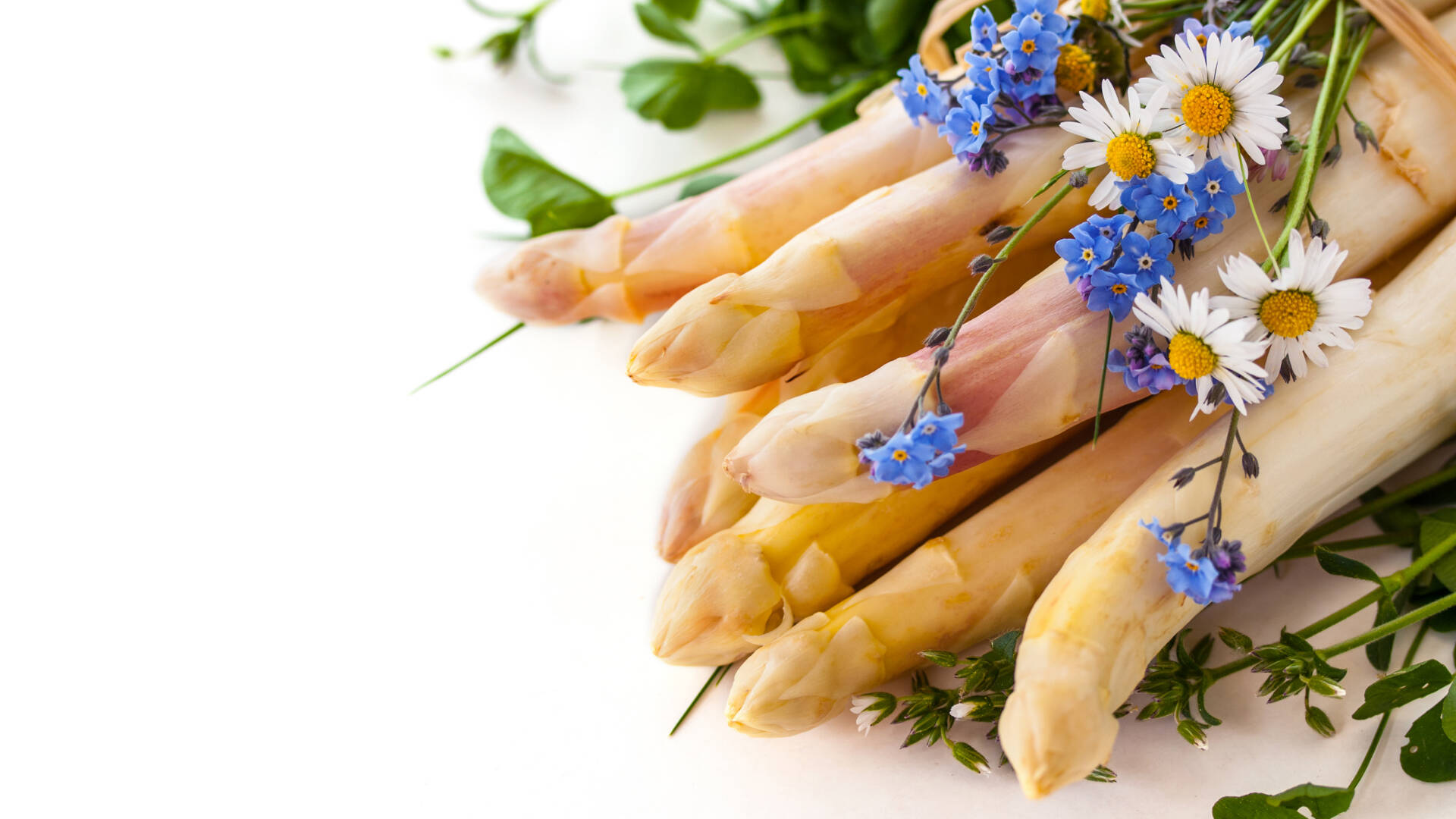 Ein Bund weißer Spargel liegt auf einem weißen Untergrund, umgeben von Blumen.