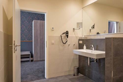 Modern gestaltetes Badezimmer in einem Doppelzimmer des Deutschherrenhofs. Helle Farben und ein großer Spiegel lassen den Raum freundlich wirken. Die Fliesen am Waschtisch sind in einem dunklem Schieferton gehalten.