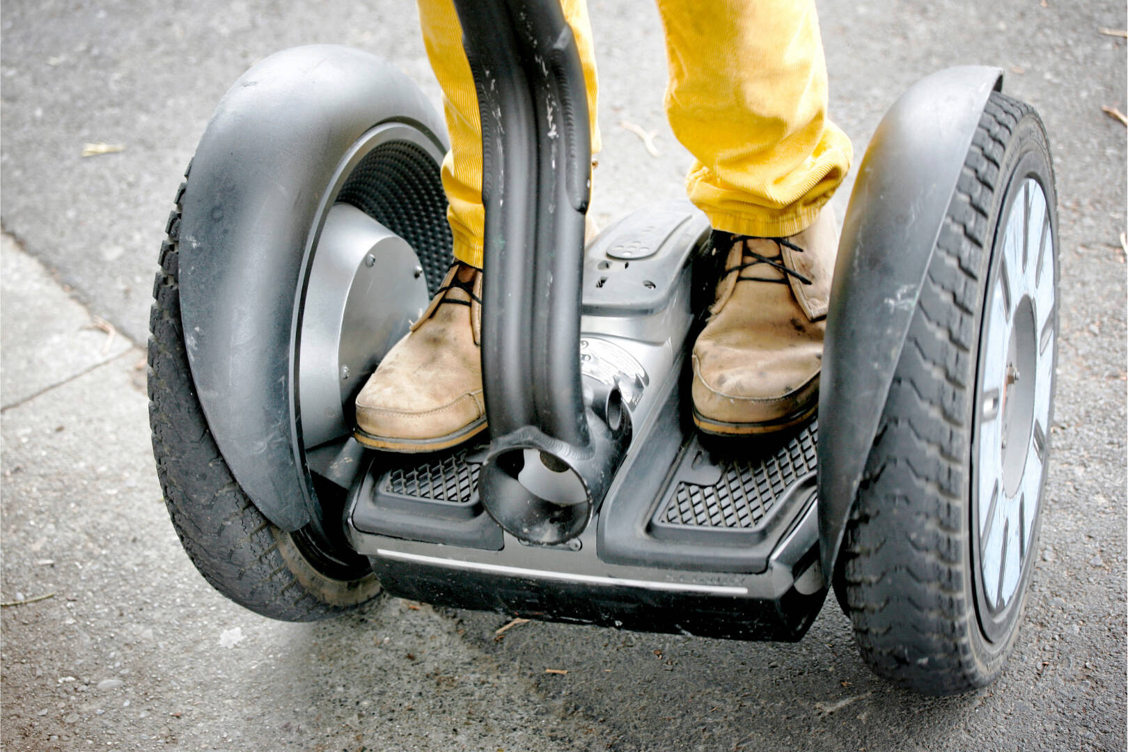 Eine Person steht auf einem Segway und trägt braune geschnürte Schuhe sowie eine gelbe Hose.