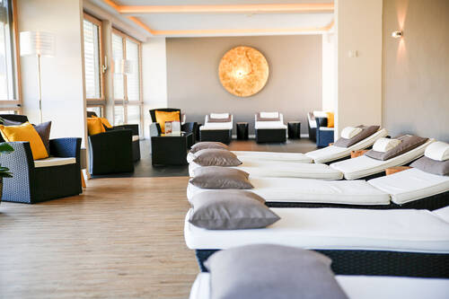 Der Ruhebereich im Wellnessbereich des Deutschherrenhofs hat einen hellen Holzboden, beige Wände und wird durch indirekte Beleuchtung in eine stimmungsvolle Atmosphäre getaucht. Mehrere Liegen stehen nebeneinander und laden zum Entspannen ein.