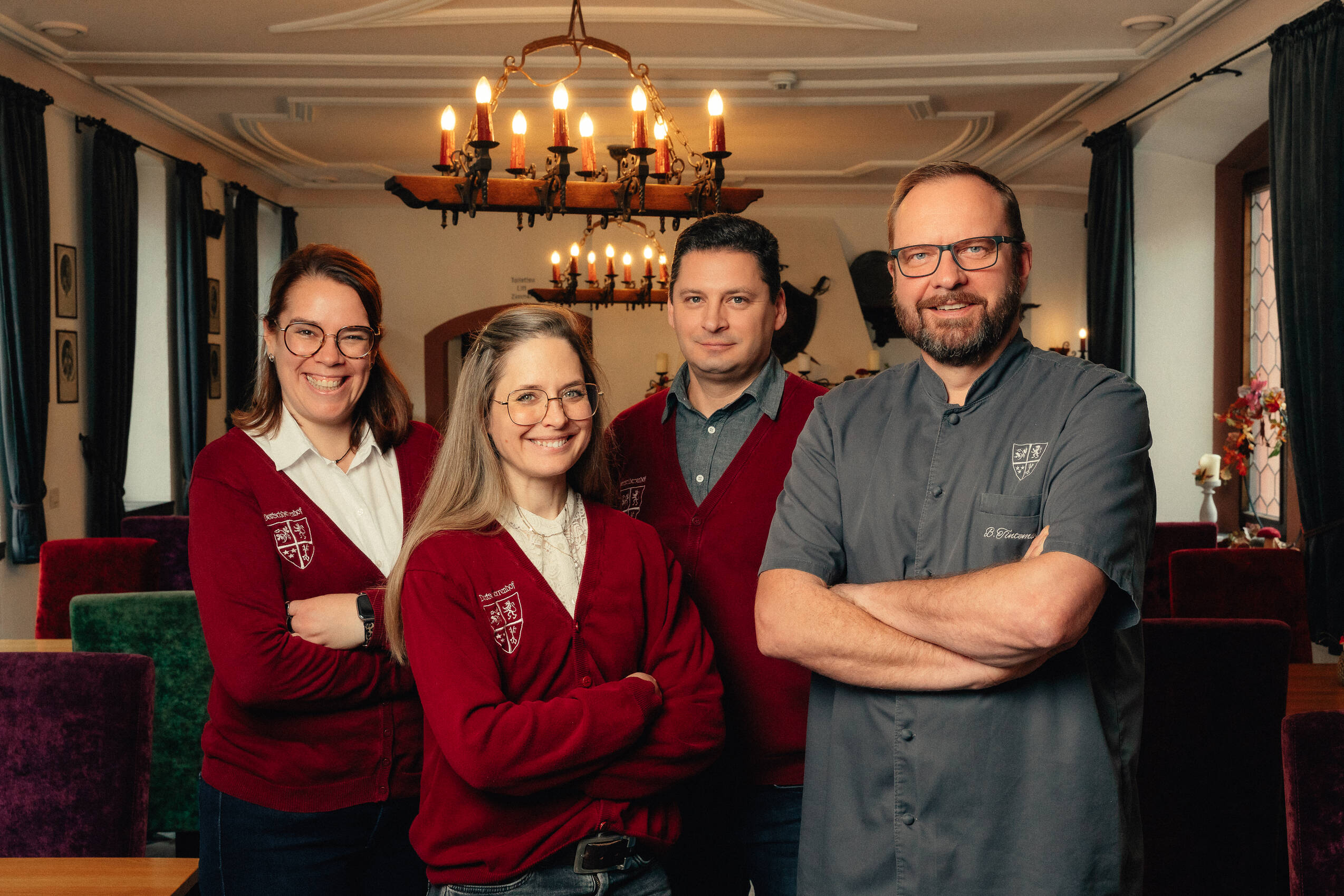 Alexandra Kropp (Gastgeberin), Terese Ott (Empfangsleitung), Krisztian Komar (Restaurantleiter) und Bernhard Tintemann (Küchenchef) stehen im Rittersaal des Deutschherrenhof und lachen in die Kamera.
