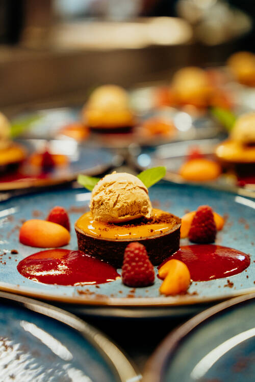 Mehrere angerichtete Desserts stehen auf großen Tellern auf einer Anrichte in der Hotelküche.