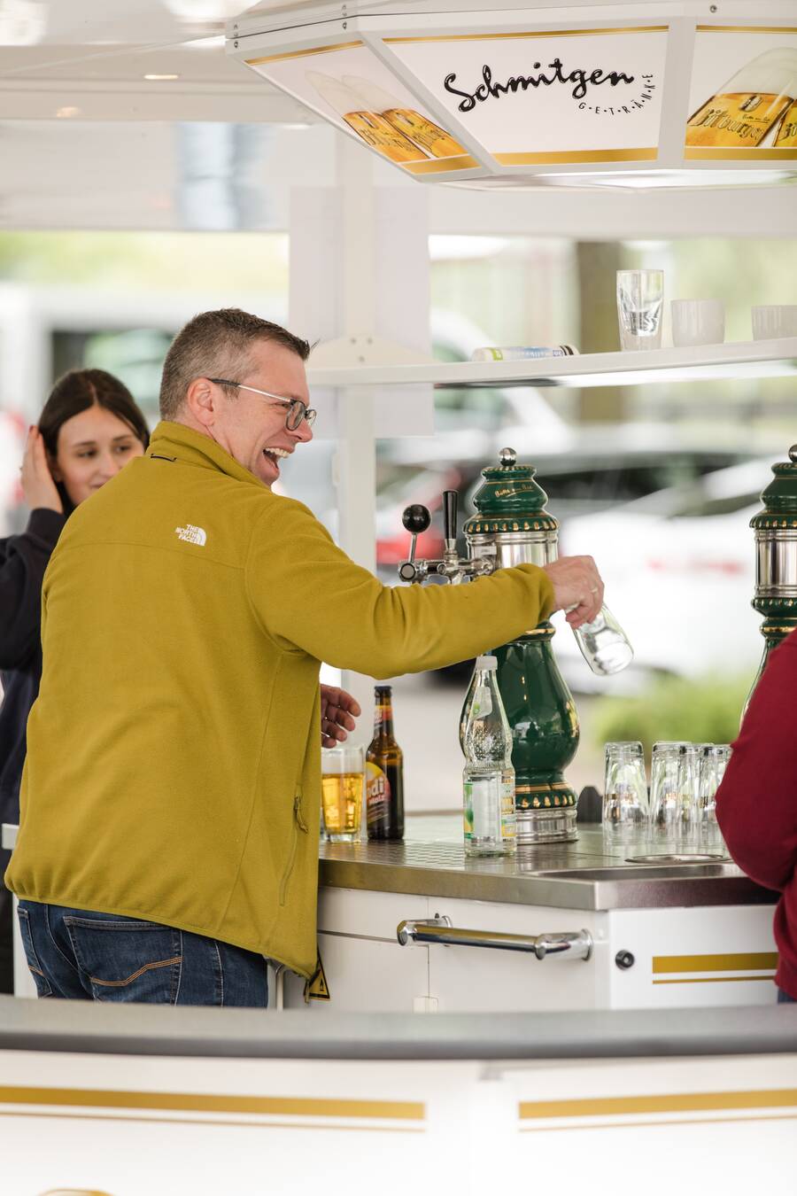 Ein Mann steht im Bierwagen und zapft ein frisches Bier. Er lacht herzlich und schaut in Richtung der Gäste.