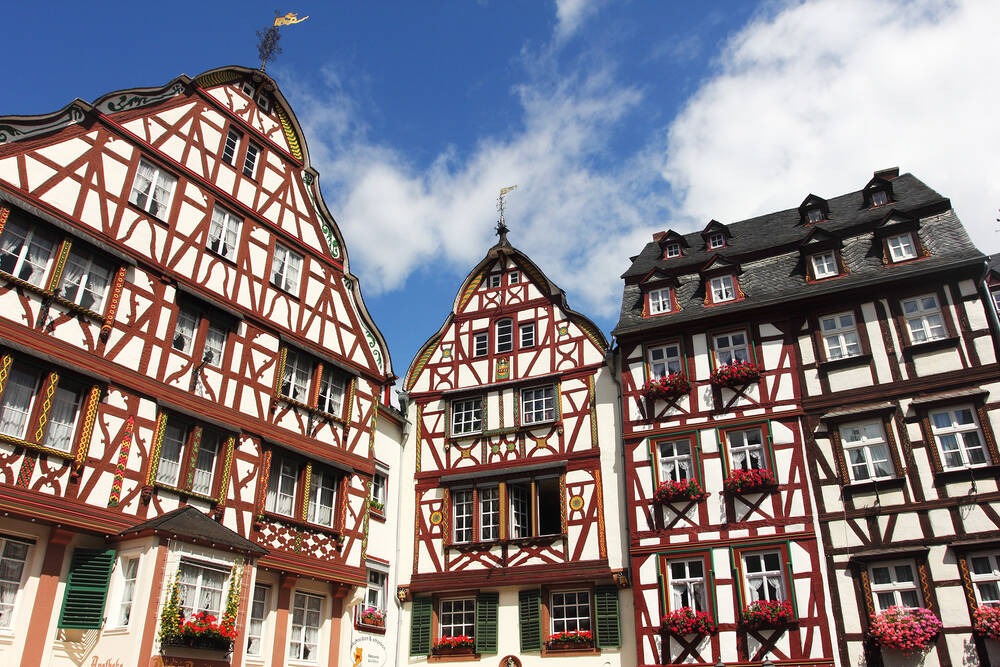 Drei Fachwerkhäuser auf dem Marktplatz in Bernkastel, von unten nach oben fotografiert vor strahlend blauem Himmel.