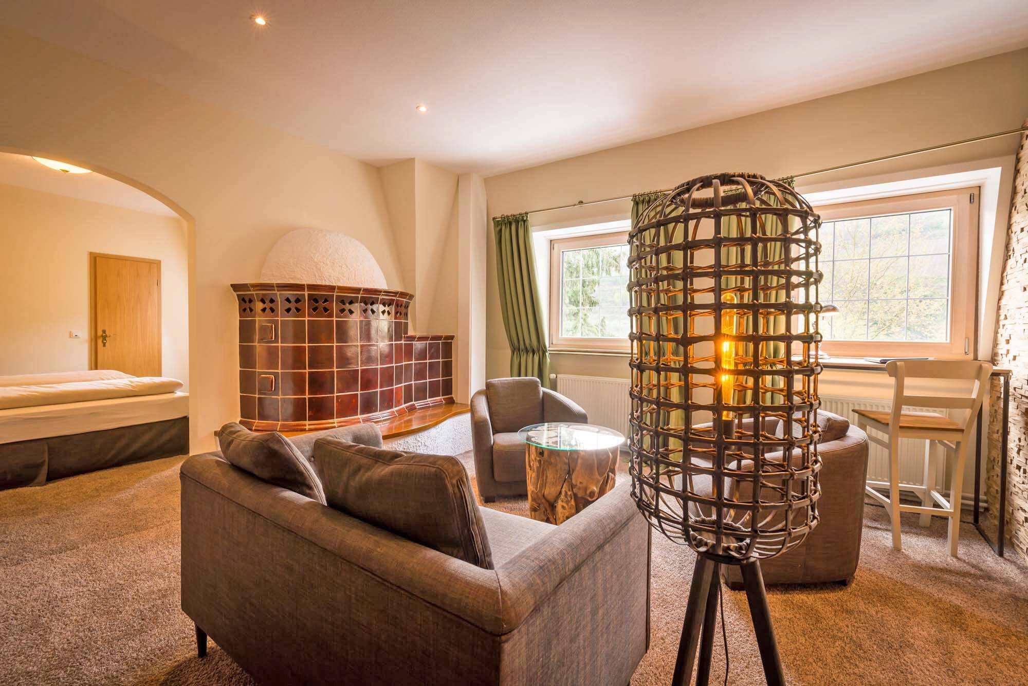 Wohnzimmer einer Suite im Deutschherrenhof mit kleiner Couch, zwei Sesseln und gemütlicher Beleuchtung. Links im Bild sieht man durch einen Durchbruch das Schlafzimmer mit Doppelbett.