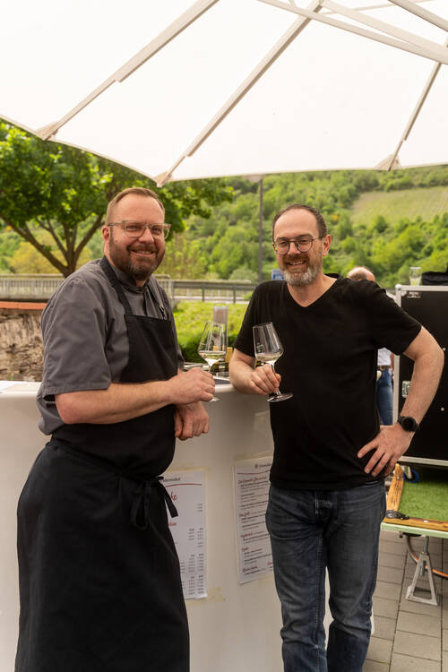 Küchenchef Bernhard Tintemann und der Winzer vom Heinrichshof stehen gemeinsam am Stehtisch und trinken ein Glas Wein.