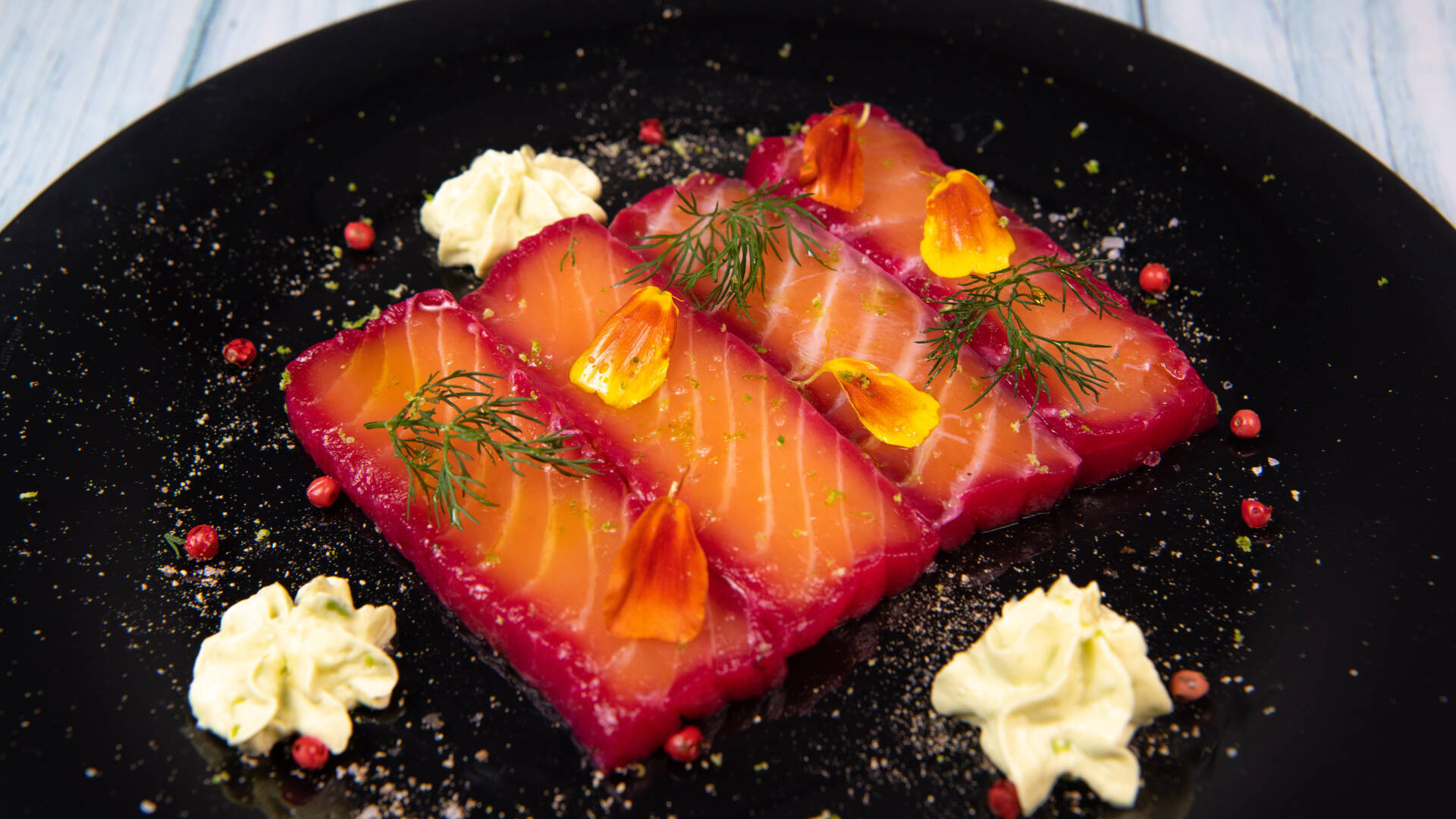 Auf einem schwarzen Teller liegt eine Portion gebeizter Lachs, appetitlich angerichtet.