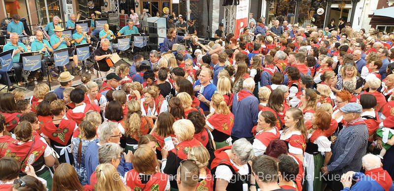 Hunderte Weinfestbesucher in Moseltracht, mit Winzerkitteln und Moselblümchen, versammeln sich auf dem Marktplatz vor der Bühne.