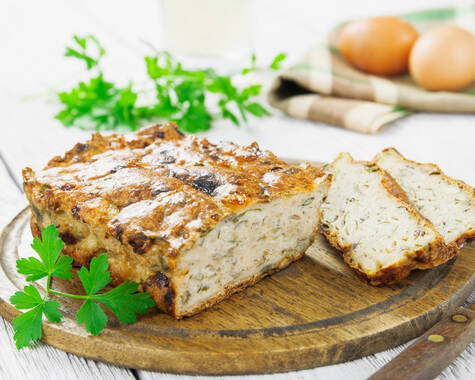 Auf einem Holzbrett liegt eine Terrine aus drei verschiedenen Kartoffelsorten, garniert mit frischem Schnittlauch. Im Hintergrund liegt ein Küchentuch, auf dem zwei Eier platziert sind.