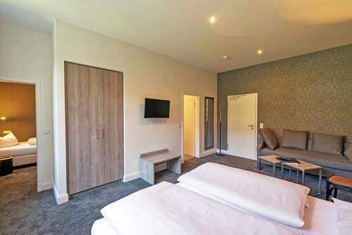 Helles Doppelzimmer im Deutschherrenhof. An der grün gemusterten Wand neben der Eingangstür steht ein Sofa mit einem kleinen Beistelltisch.