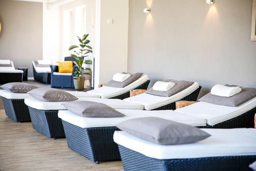 Der Ruhebereich im Wellnessbereich des Deutschherrenhofs hat einen hellen Holzboden, beige Wände und wird durch indirekte Beleuchtung in eine stimmungsvolle Atmosphäre getaucht. Mehrere Liegen stehen nebeneinander und laden zum Entspannen ein.