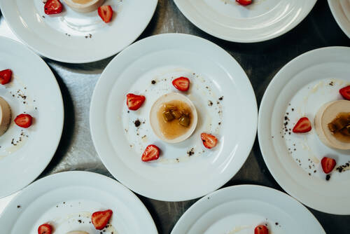 Mehrere Teller mit Nachspeise stehen auf einer Anrichte in der Hotelküche. Die Desserts sind mit frischen Erdbeeren dekoriert.