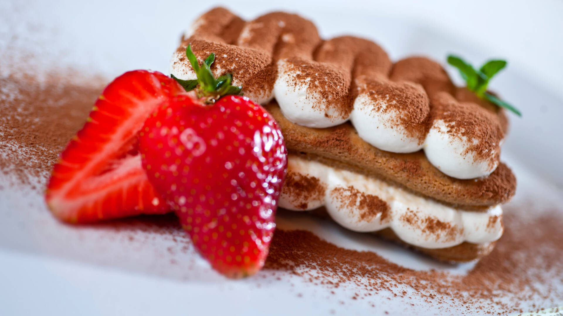 Zwei aufgeschnittene Erdbeerhälften lehnen an einem Stück Tiramisu und dienen als fruchtige Dekoration.