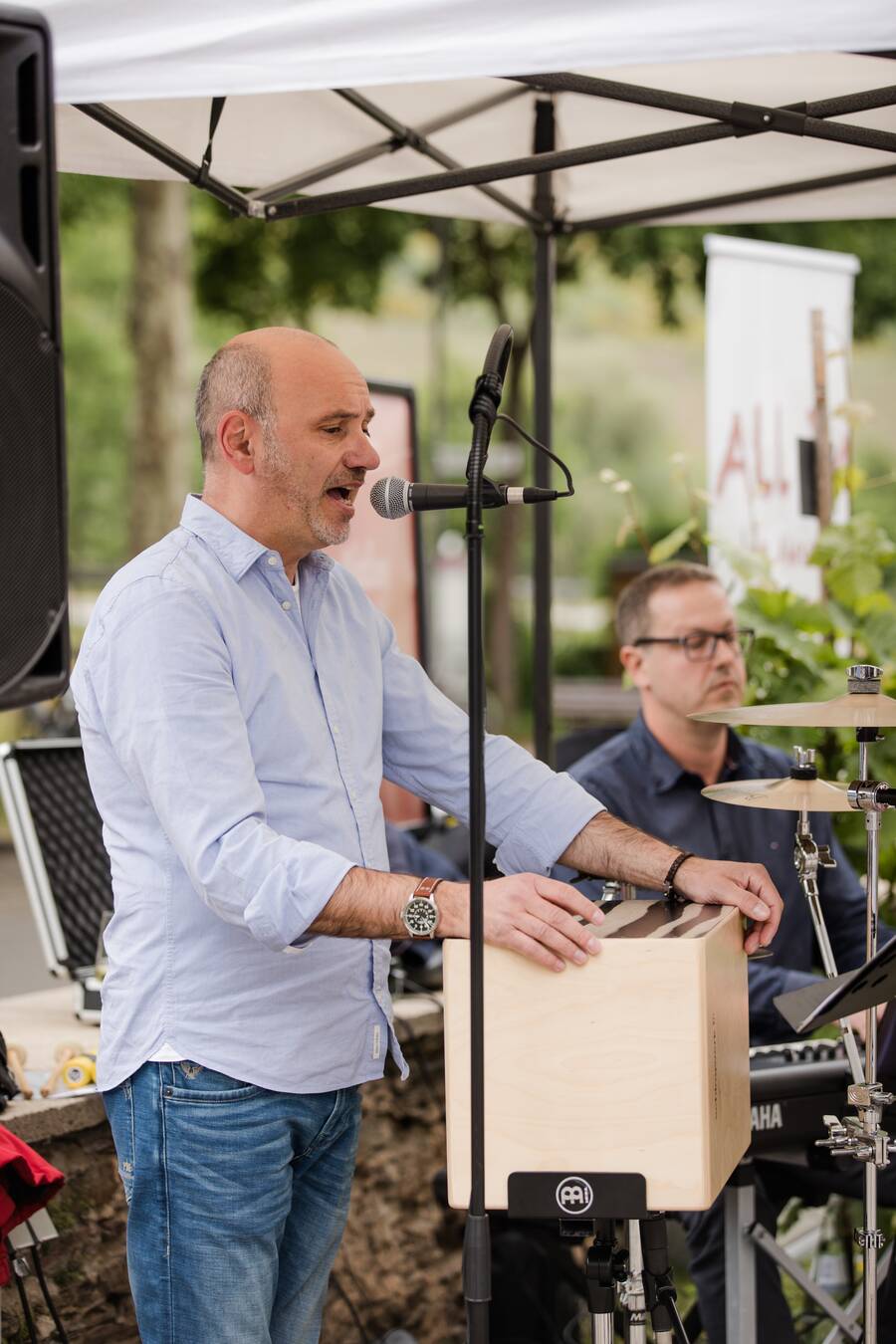 Ein Musiker von All-In-das Akustiktrio steht vor seinem Instrument und singt in ein Mikrofon.