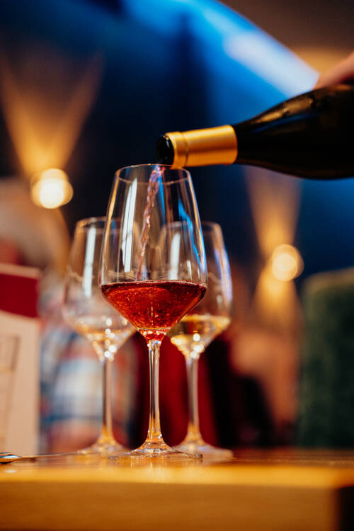 Roséwein wird aus einer Flasche in ein Weinglas auf einem gedeckten Tisch eingeschenkt.