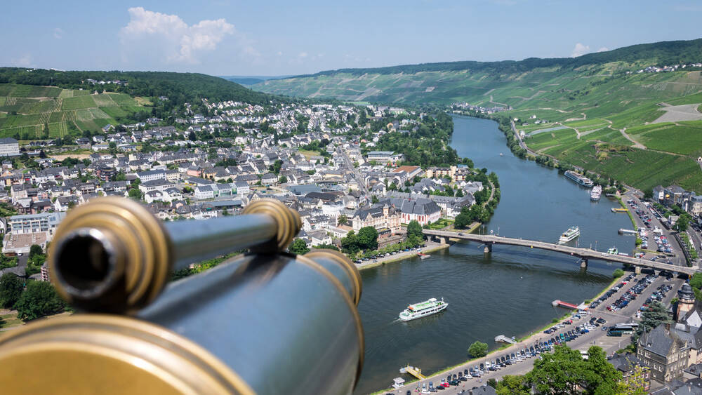 Ausblick auf Bernkastel-Kues mit zwei Schiffen auf der Mosel. Im Vordergrund steht ein Fernrohr.