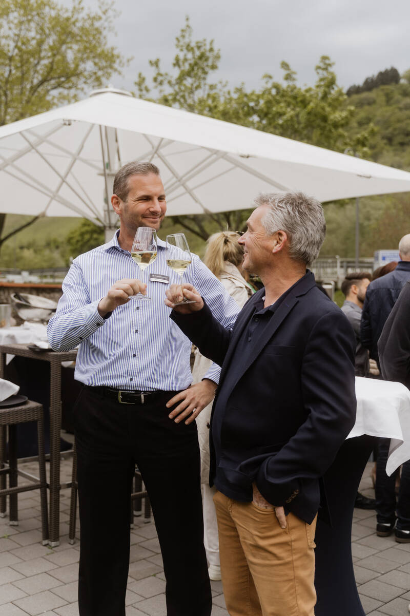 Restaurantleiter Martin und ein Gast stoßen mit einem Glas Sekt in der Hand an und lachen sich gegenseitig an.