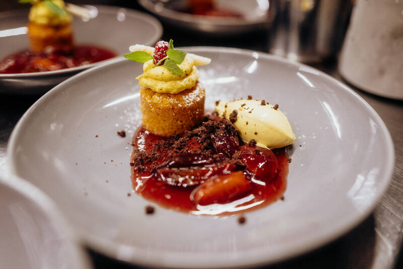 Mehrere angerichtete Desserts stehen auf großen Tellern auf einer Anrichte in der Hotelküche.