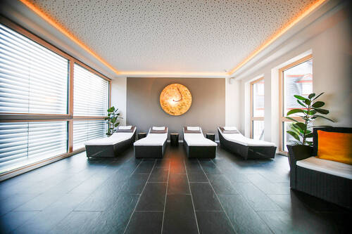 Blick in den Wellnessbereich des Deutschherrenhofs. Die indirekte Beleuchtung und die Holzverkleidungen verleihen dem Raum eine goldene Farbstimmung. Vier Liegen stehen nebeneinander am Kopfende des Raums. An der Wand ist ein indirekt beleuchtetes, goldenes Kunstwerk zu sehen.