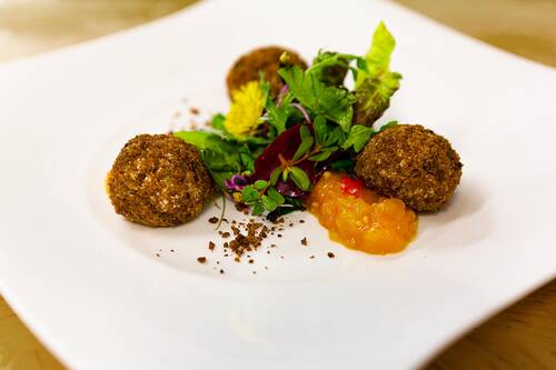 Detailaufnahme eines Gerichts mit Ziegenfrischkäsebällchen, angerichtet mit Salat und einem Obst-Chutney.