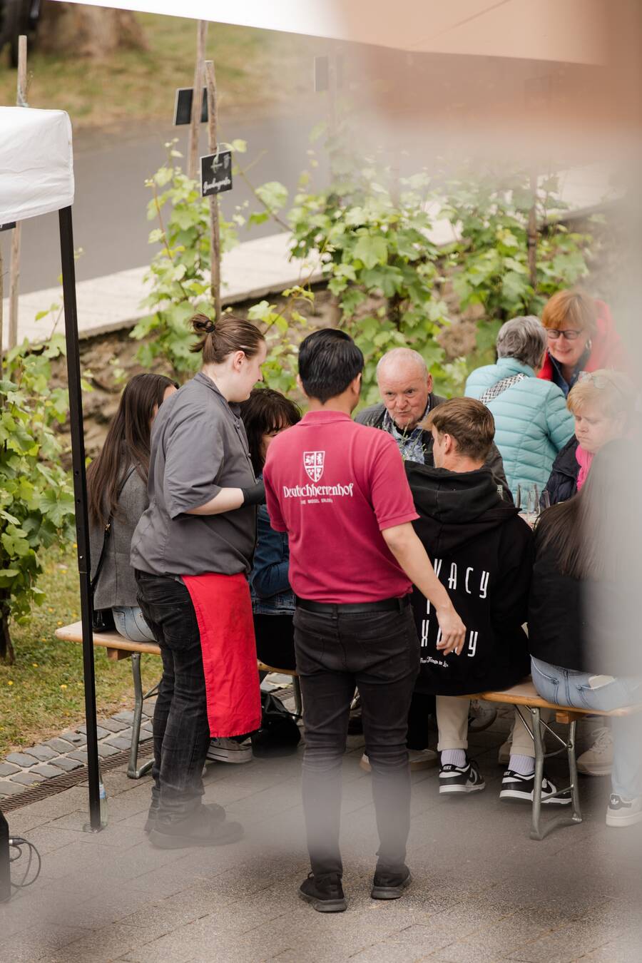 Zwei Mitarbeiter des Hotels bedienen mehrere Menschen, die auf einer Bierzeltgarnitur sitzen.